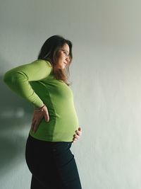 Side view of pregnant woman standing by wall