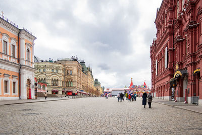 People on street amidst buildings in city against sky