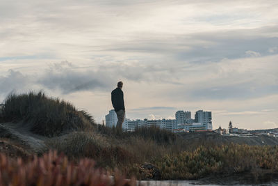 Rear view of man looking at cityscape against sky