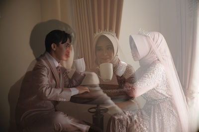 Multiple exposure image of bridegroom holding coffee cup sitting by table