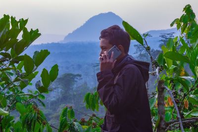 Side view of young man standing on mountain against sky