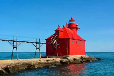 Lighthouse by sea against clear blue sky