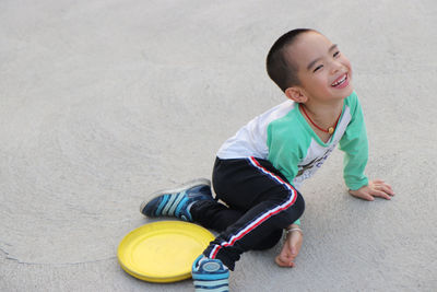 Portrait of smiling boy sitting with plastic disc on footpath at park