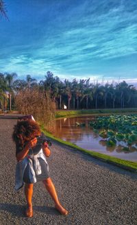 Rear view of woman walking by trees against sky