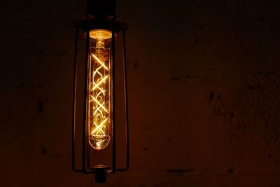 Close-up up illuminated light bulb against wall