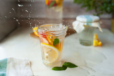 Homemade lemonade in  wet glass cup with water drops with a jug of citrus drink on a wooden