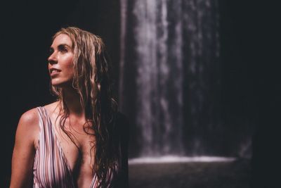 Woman looking away while standing against waterfall