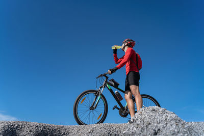 Low angle view of man riding bicycle against clear blue sky