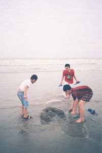 Boys standing on beach against clear sky