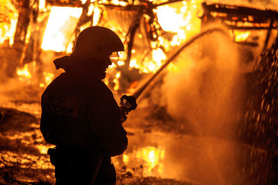 Rear view of silhouette firefighter extinguishing fire