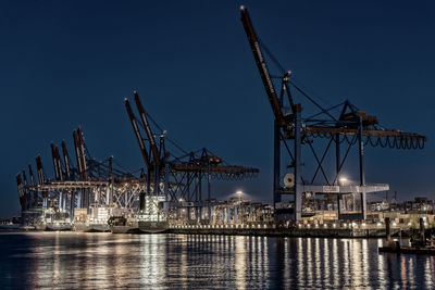 Cranes at harbor against sky at night