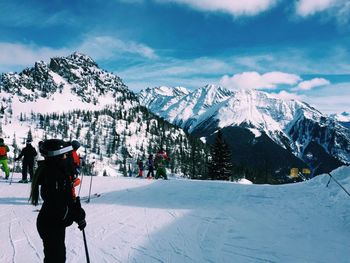 People skiing on snow covered field against mountains