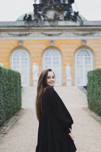 Portrait of young woman standing against building