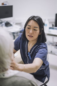 Female otolaryngologist examining throat of senior patient in medical clinic