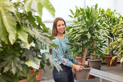 Portrait of smiling young woman standing against potted plants