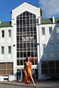 Glamorous urban photography, chic image of model in golden silk dress outdoors posing near building 