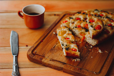 Homemade italian focaccia, with tomato and olive oil and coffee on a rustic wooden background.