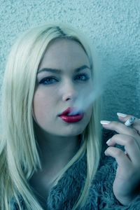 Close-up portrait of young woman smoking cigarette while standing by wall