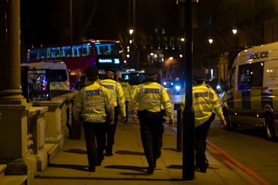 Rear view of people walking on illuminated street at night