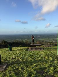 Woman standing on bench over landscape against sky