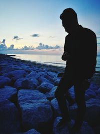 Silhouette man standing on rock at beach against sky during sunset