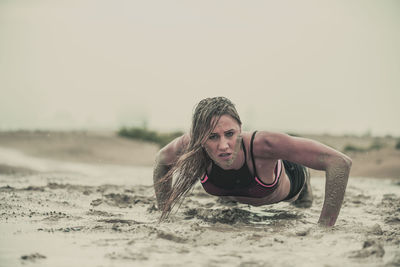 Portrait of young woman on sand at beach against sky