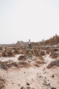 Man standing on rock in desert against clear sky