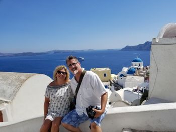 Portrait of smiling mature couple in town against sea during sunny day