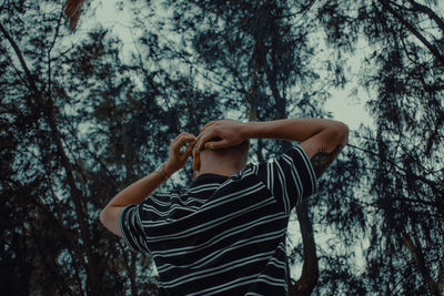 Rear view of man with hand in hair while standing in forest