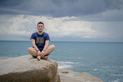 Full length of man on rock in sea against sky