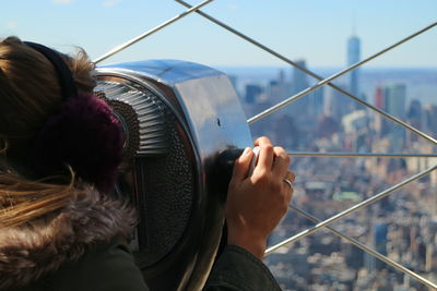 Rear view of woman looking through coin-operated binoculars against cityscape