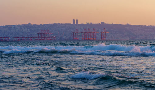 Sea waves rushing towards buildings in city during sunset