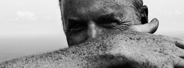 Close-up portrait of man covering face with hand against sky