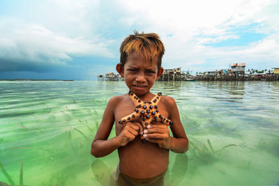 Portrait of boy standing in sea against sky