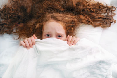 Sad little girl afraid sleeping and pulling quilt on head.
