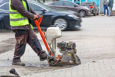 A road worker is repairing the carriageway of a city street, cutting out a bad section with a cutter