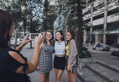 Side view of woman photographing friends with smart phone on sidewalk