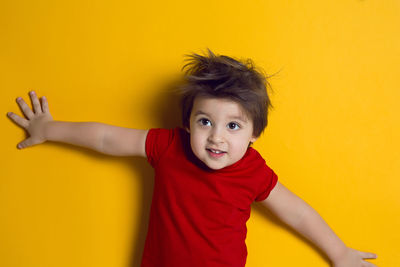 Cheerful baby boy in red t-shirt stands on yellow background