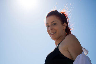 Below view of happy redhead woman against the sky looking at camera.