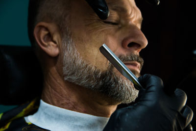 Cropped hands of barber cutting beard of man at salon