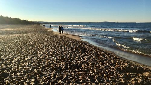 People walking on beach against clear sky