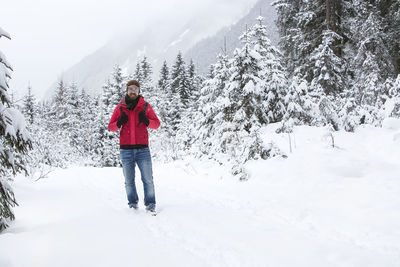 Young man with red jacket is hiking in wintry forest landscape
