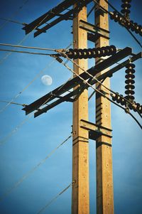 Low angle view of electricity pylon against blue sky