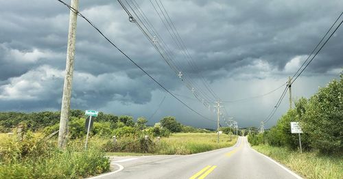 Road by electricity pylon against sky