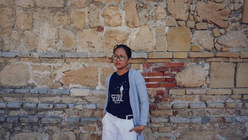 Portrait of young woman standing against brick wall