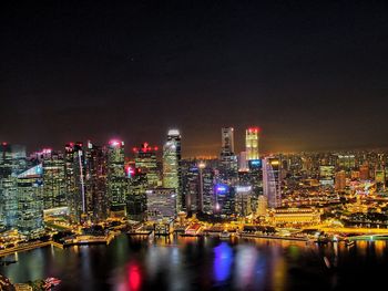 Illuminated buildings by river against sky at night