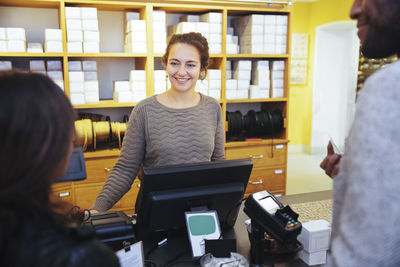 Smiling young female cashier looking at customer standing in furniture store