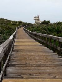 Wooden footbridge leading to water against sky