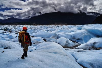 Rear view of man walking on snowcapped mountain against sky