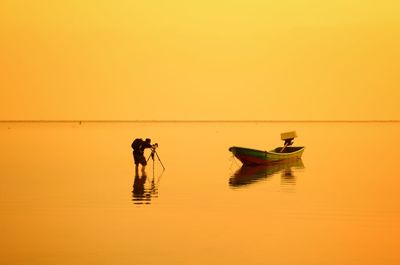 People in boat on sea against orange sky